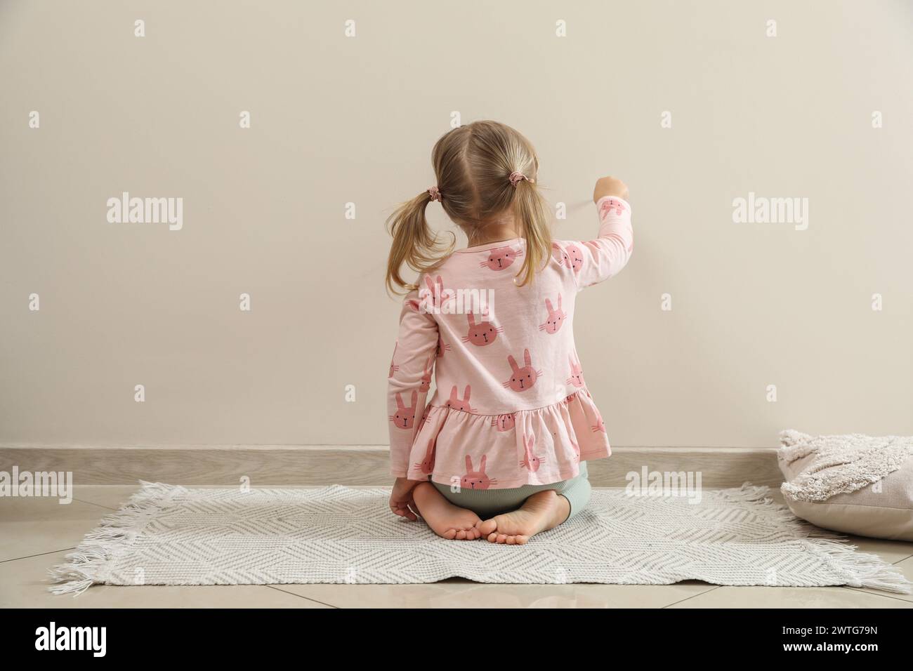 Little girl drawing on beige wall indoors, back view. Child`s art Stock Photo